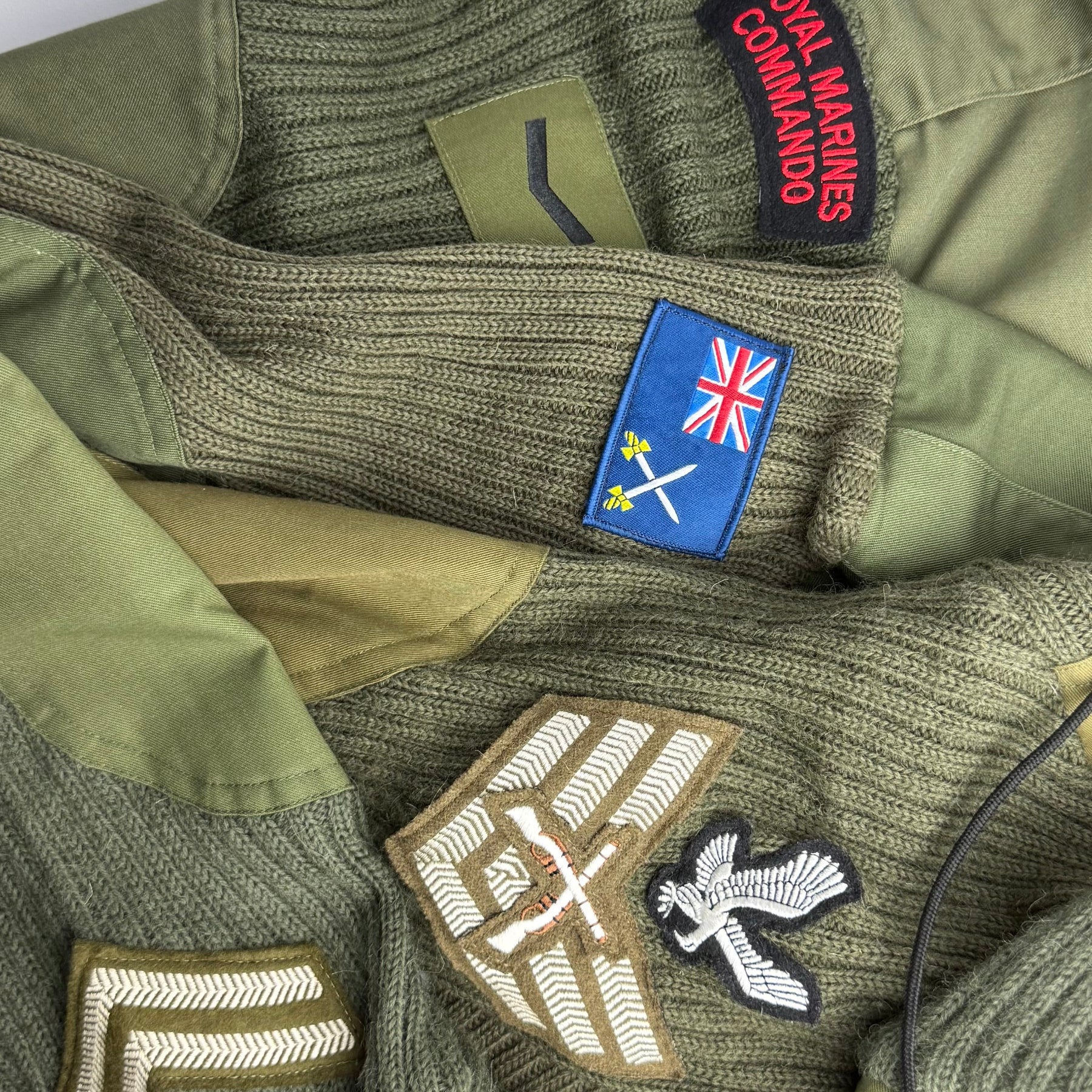 Close-up of green military wool jumper sleeves with various patches including a Royal Marines Commando patch.