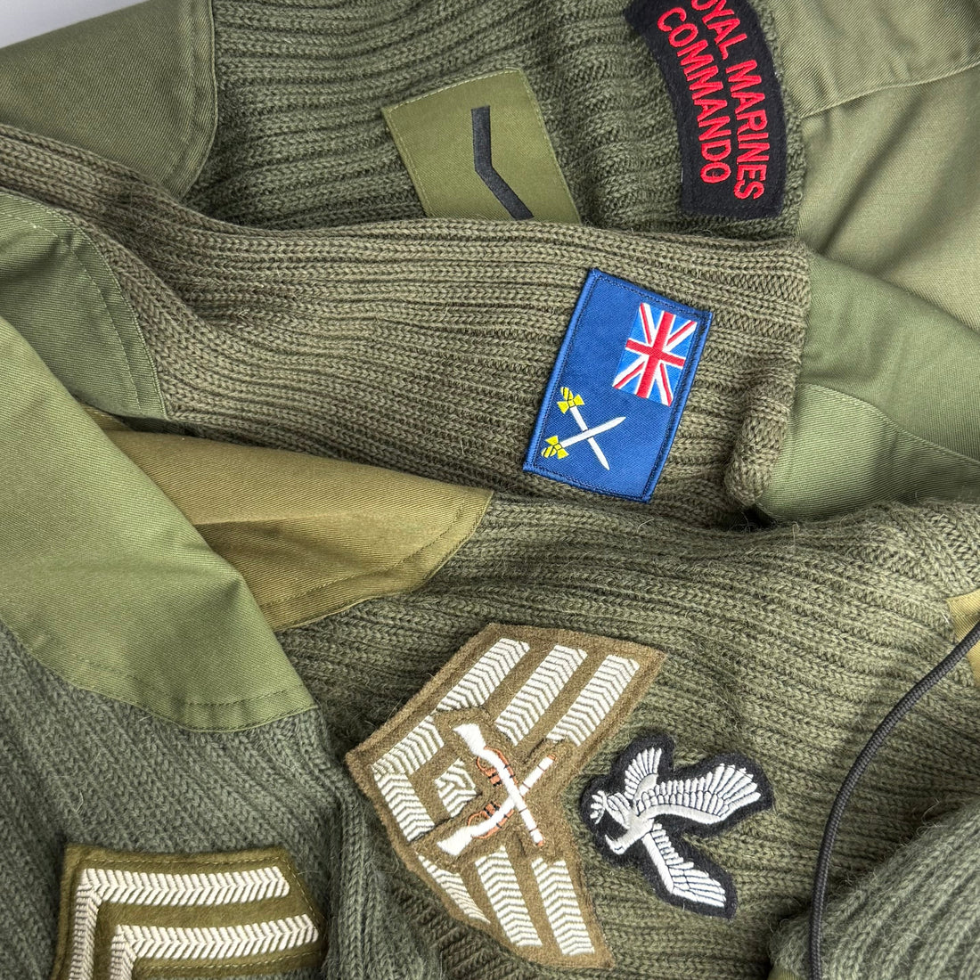 Close-up of green military wool jumper sleeves with various patches including a Royal Marines Commando patch.